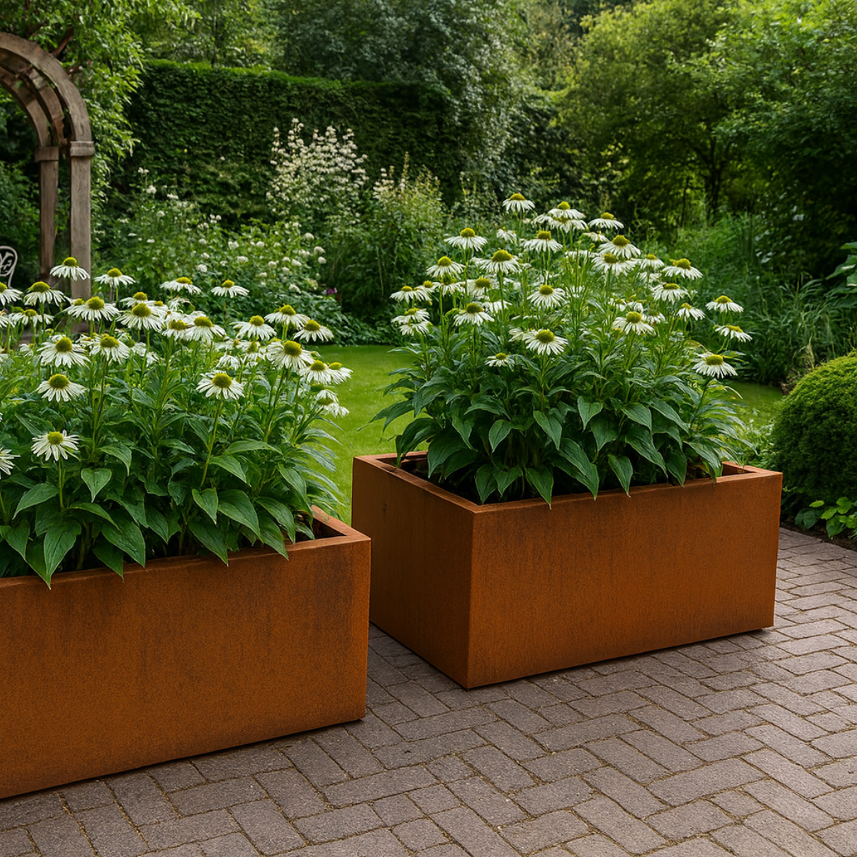 Twee cortenstalen plantenbakken gevuld met witte bloemen in een sfeervolle tuin met bestrating.