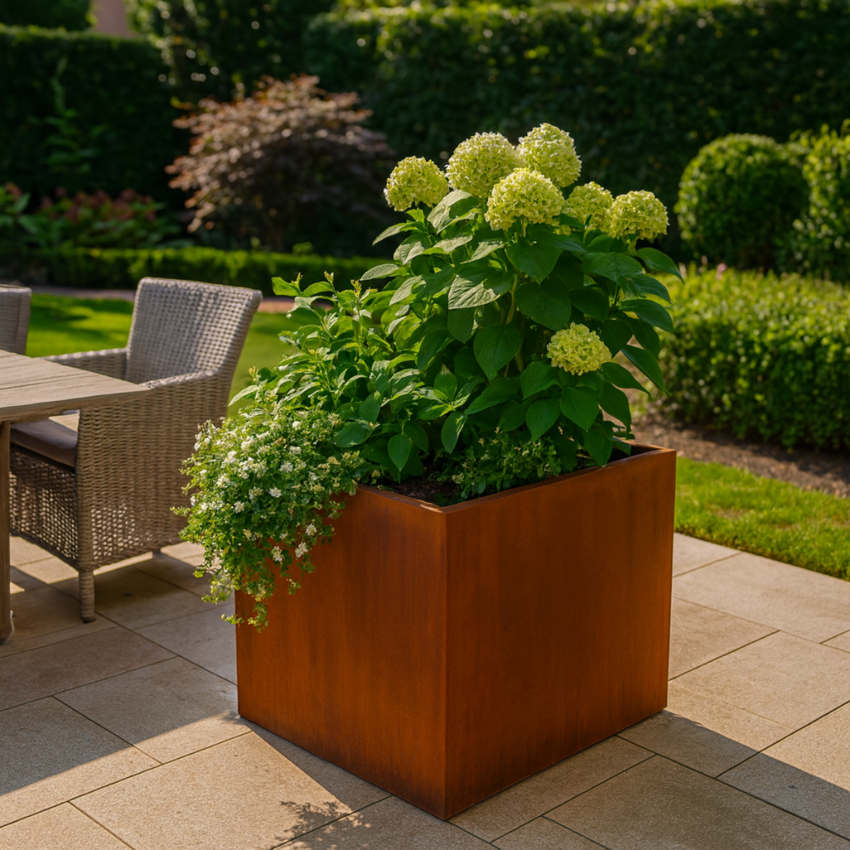 Cortenstalen plantenbak gevuld met lichtgroene hortensia's en witte bloemen in een sfeervolle tuin met een betegeld terras.