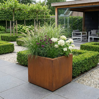 Vierkante Cortenstalen plantenbak met siergrassen en witte hortensia's op een modern terras.