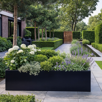 Lage zwarte rechthoekige plantenbak gevuld met witte hortensia's, buxusbollen en paarse bloeiers op een ruimtelijk terras met bomen.